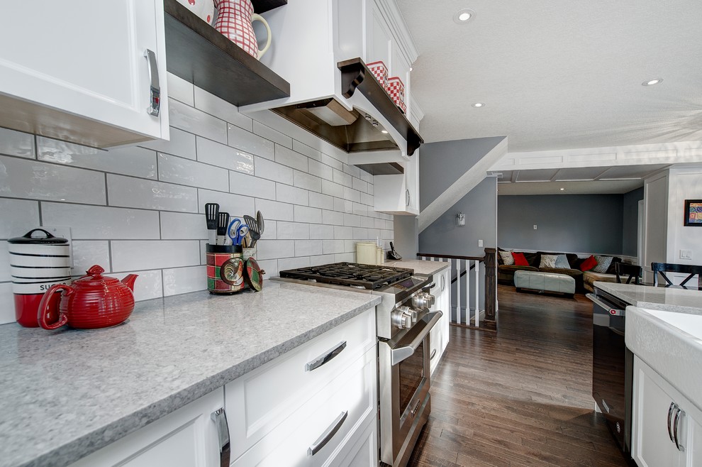 Eat-in kitchen - craftsman l-shaped medium tone wood floor and brown floor eat-in kitchen idea in Calgary with a farmhouse sink, shaker cabinets, white cabinets, quartz countertops, white backsplash, subway tile backsplash, stainless steel appliances and an island