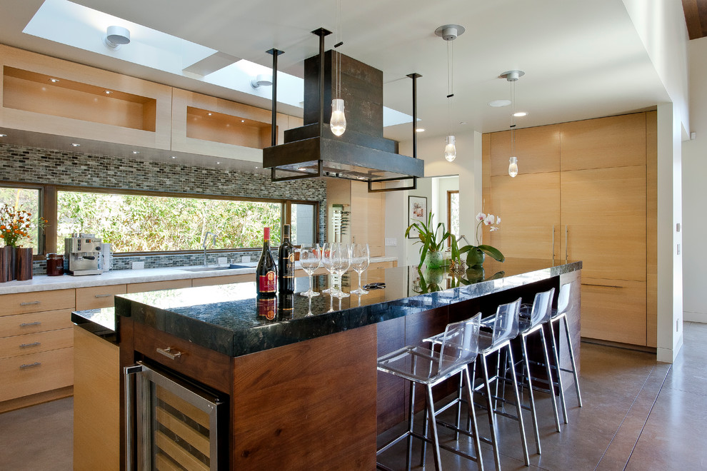 Modern inredning av ett kök, med en undermonterad diskho, släta luckor, skåp i ljust trä, flerfärgad stänkskydd, stänkskydd i mosaik, integrerade vitvaror, en köksö och brunt golv