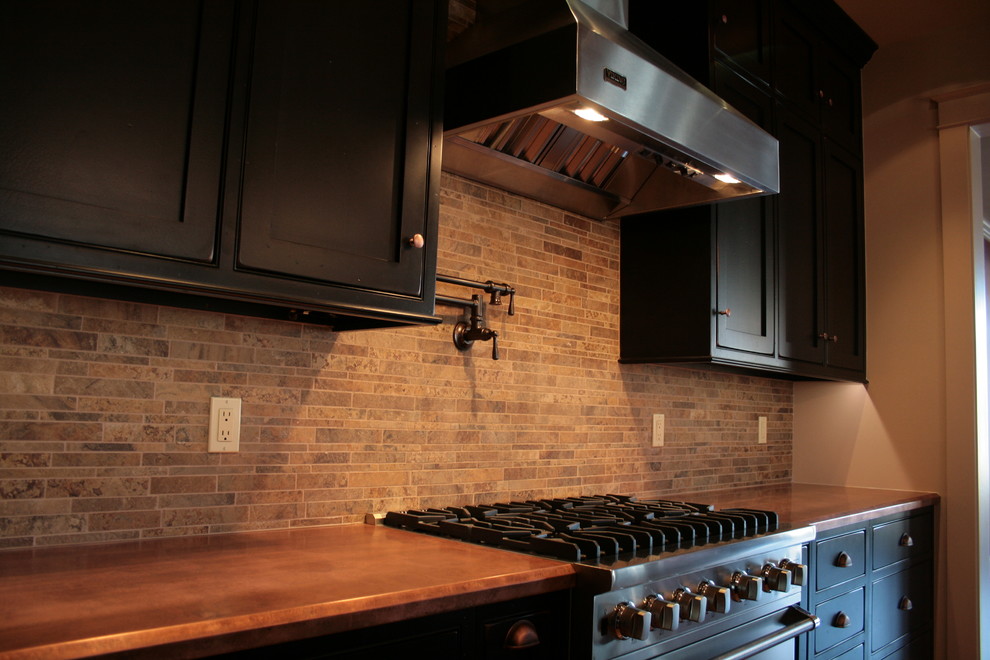 Esempio di una cucina eclettica di medie dimensioni con ante a filo, ante nere, top in rame, paraspruzzi beige, paraspruzzi con piastrelle in ceramica, elettrodomestici in acciaio inossidabile e pavimento in legno massello medio