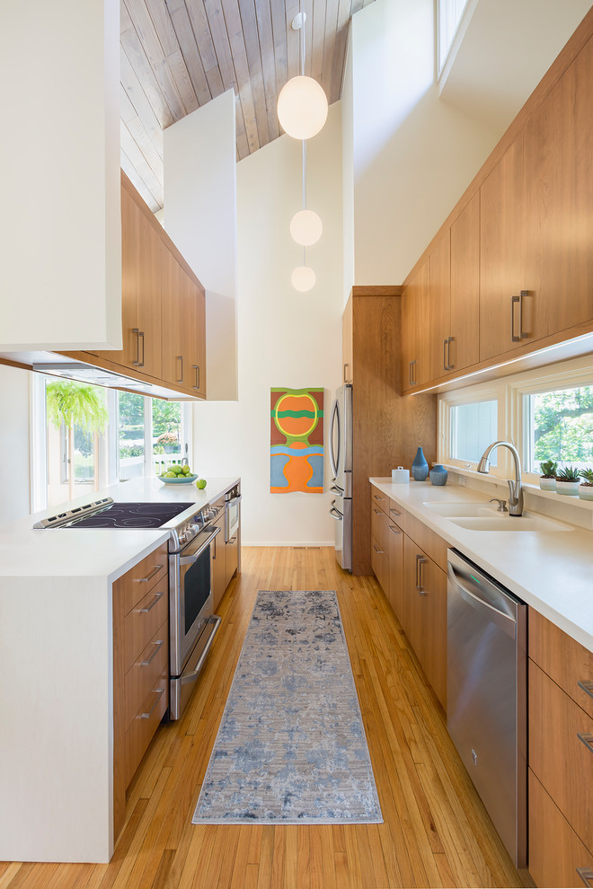 Medium sized midcentury galley enclosed kitchen in Minneapolis with an integrated sink, flat-panel cabinets, brown cabinets, composite countertops, stainless steel appliances, light hardwood flooring, an island, brown floors and white worktops.