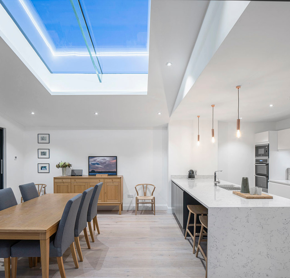 This is an example of a large contemporary kitchen/diner in Dublin with flat-panel cabinets, white cabinets, light hardwood flooring and an island.
