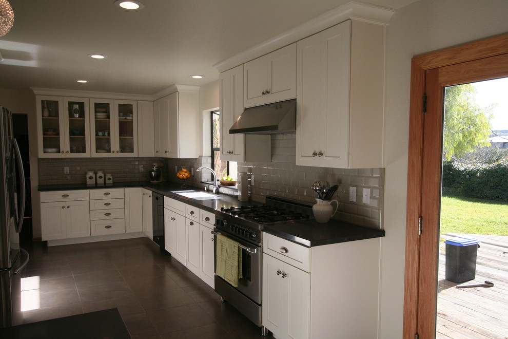 Example of a mid-sized classic u-shaped travertine floor eat-in kitchen design in San Francisco with an undermount sink, recessed-panel cabinets, beige cabinets, laminate countertops, gray backsplash, ceramic backsplash and stainless steel appliances