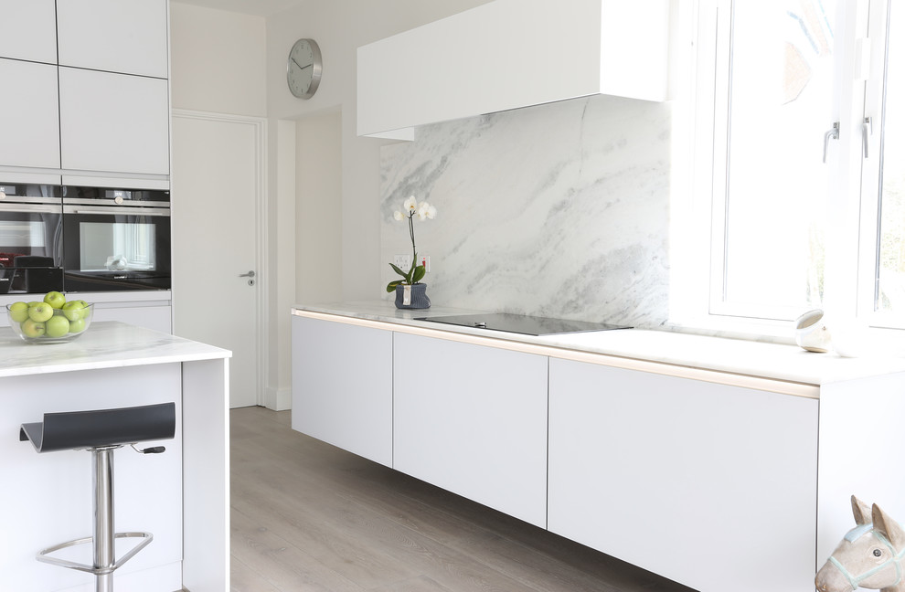 Photo of a contemporary kitchen in Dublin with flat-panel cabinets, white cabinets, marble worktops, stone slab splashback, stainless steel appliances and light hardwood flooring.