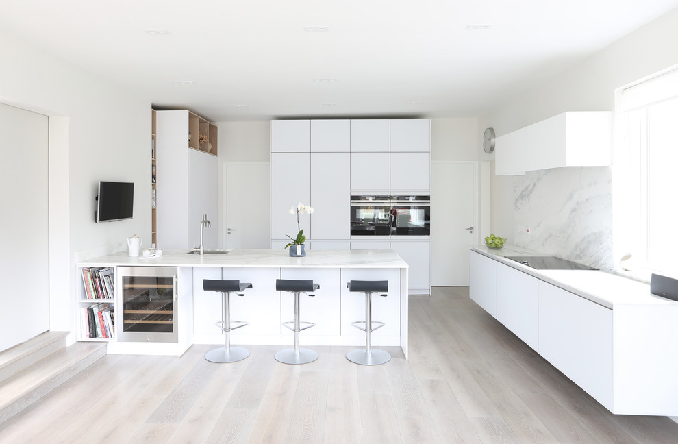 Immagine di una cucina minimalista con ante lisce, ante bianche, top in marmo, paraspruzzi in lastra di pietra, elettrodomestici in acciaio inossidabile e parquet chiaro