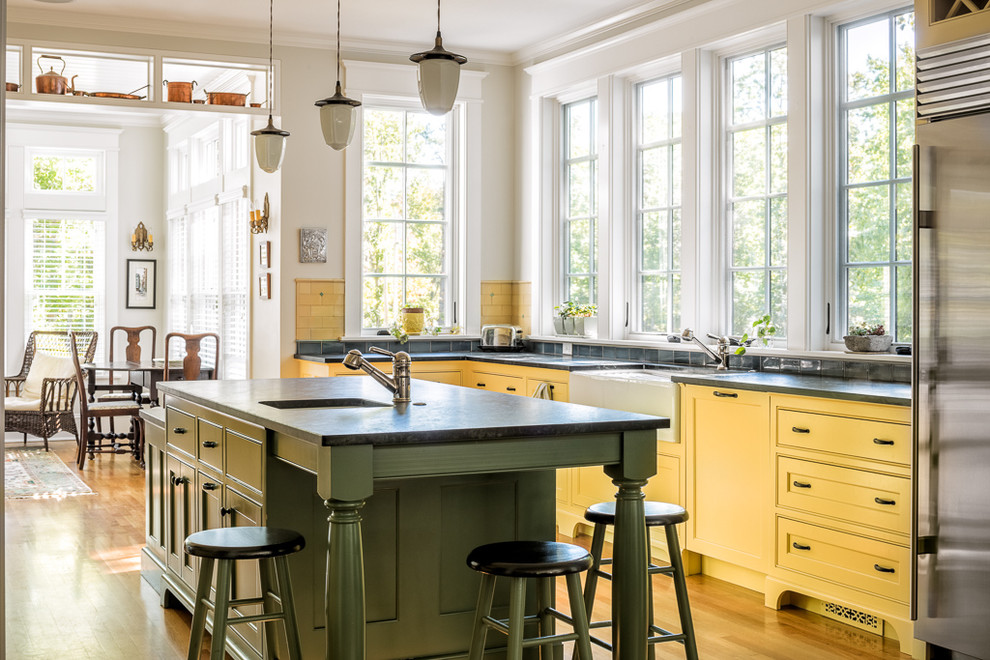 Klassische Küche in L-Form mit Landhausspüle, Kassettenfronten, gelben Schränken, Küchenrückwand in Blau, hellem Holzboden, Kücheninsel und braunem Boden in Portland Maine