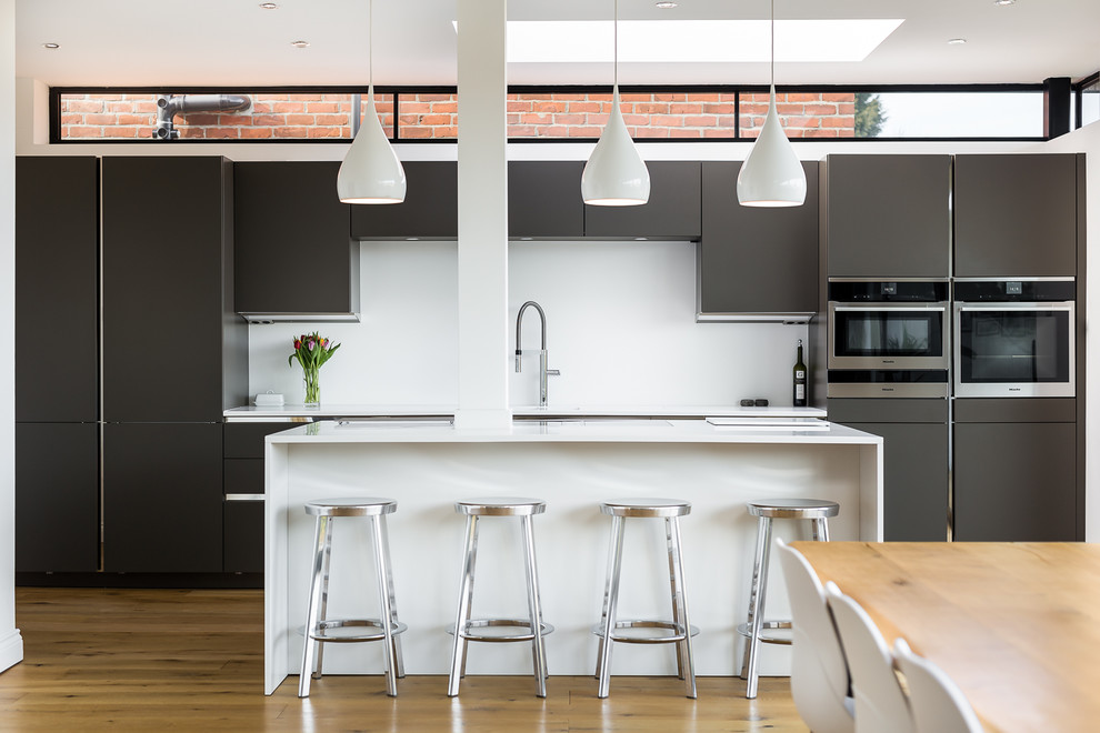 Inspiration for a medium sized contemporary single-wall kitchen/diner in Other with flat-panel cabinets, grey cabinets, white splashback, stainless steel appliances, light hardwood flooring, an island, white worktops, a submerged sink, quartz worktops and beige floors.