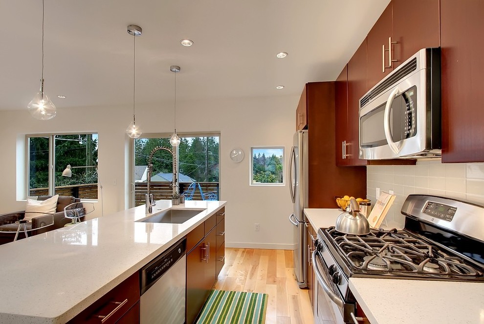 Design ideas for a contemporary galley open plan kitchen in Seattle with flat-panel cabinets, stainless steel appliances, a single-bowl sink, dark wood cabinets and white splashback.
