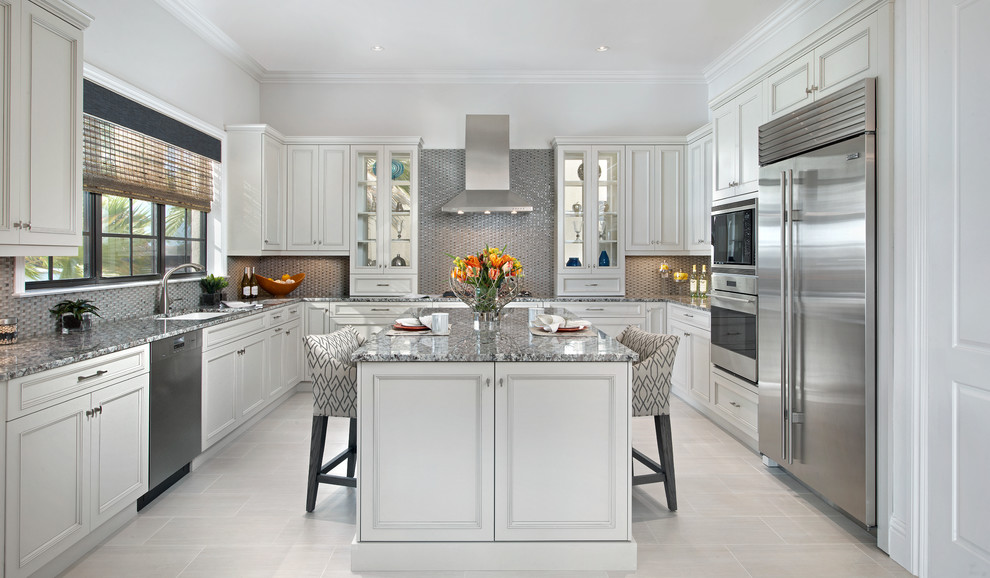 Ejemplo de cocinas en U tradicional con puertas de armario blancas, encimera de granito, electrodomésticos de acero inoxidable, suelo de baldosas de porcelana, una isla, fregadero bajoencimera, armarios con rebordes decorativos, salpicadero metalizado y salpicadero de metal