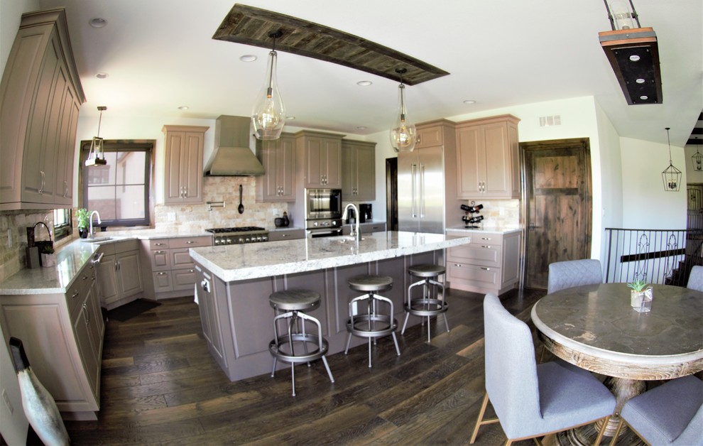 Bild på ett stort lantligt grå grått kök, med en nedsänkt diskho, skåp i shakerstil, grå skåp, granitbänkskiva, beige stänkskydd, stänkskydd i porslinskakel, rostfria vitvaror, mörkt trägolv, en köksö och brunt golv