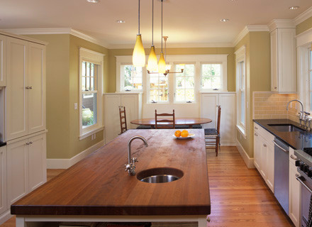 Inredning av ett klassiskt mellanstort kök och matrum, med en undermonterad diskho, luckor med infälld panel, vita skåp, stänkskydd i keramik, rostfria vitvaror, mellanmörkt trägolv och en köksö