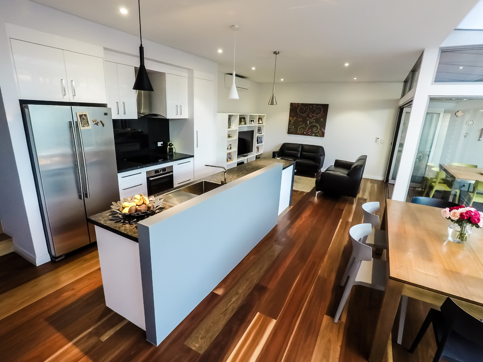 Photo of a small contemporary u-shaped kitchen in Perth with a single-bowl sink, white cabinets, granite worktops, black splashback, glass sheet splashback, stainless steel appliances, light hardwood flooring, multiple islands and black worktops.