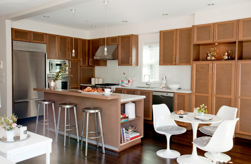 Große Klassische Wohnküche in L-Form mit Schrankfronten mit vertiefter Füllung, hellbraunen Holzschränken, Küchenrückwand in Weiß, Küchengeräten aus Edelstahl und dunklem Holzboden in Vancouver