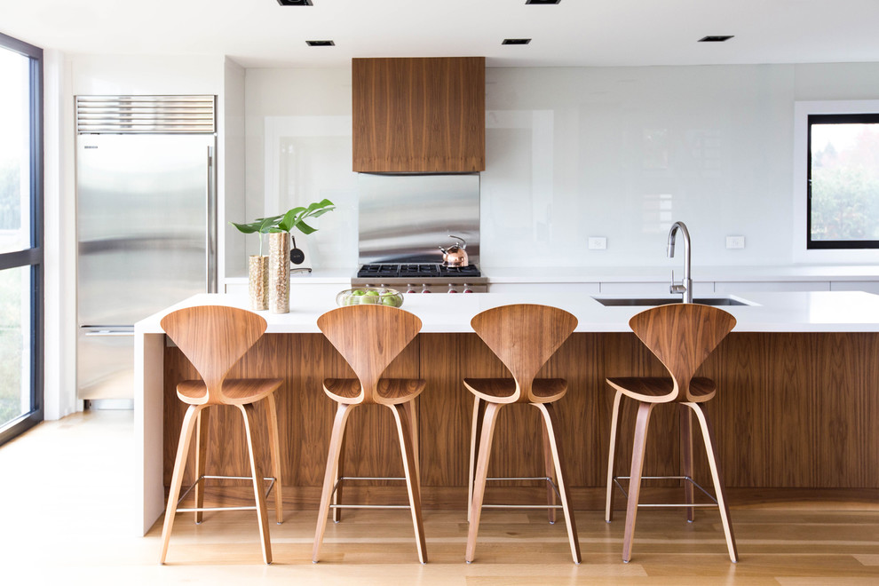 Immagine di un cucina con isola centrale moderno con lavello sottopiano, paraspruzzi a effetto metallico, elettrodomestici in acciaio inossidabile, parquet chiaro e pavimento beige