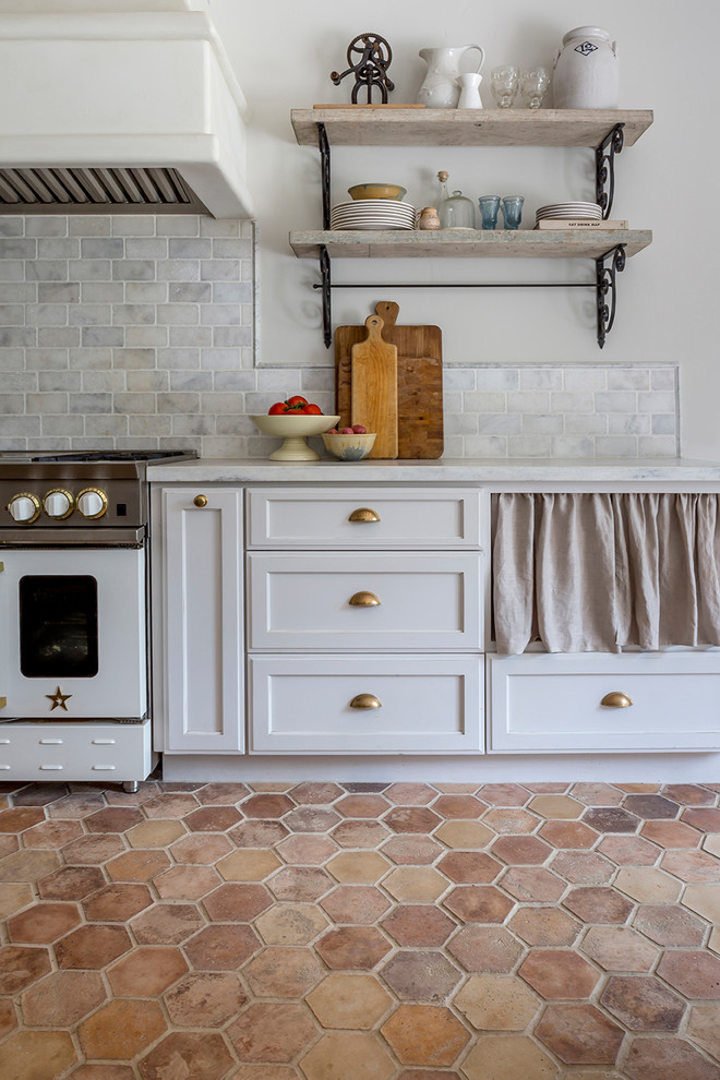 Bild på ett mellanstort rustikt kök, med en enkel diskho, luckor med upphöjd panel, vita skåp, marmorbänkskiva, grått stänkskydd, stänkskydd i keramik, rostfria vitvaror, cementgolv, en köksö och rött golv