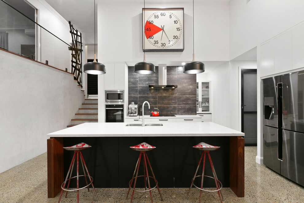 Immagine di un cucina con isola centrale industriale con lavello sottopiano, ante bianche, paraspruzzi marrone, elettrodomestici in acciaio inossidabile, pavimento beige, top bianco e pavimento in cemento
