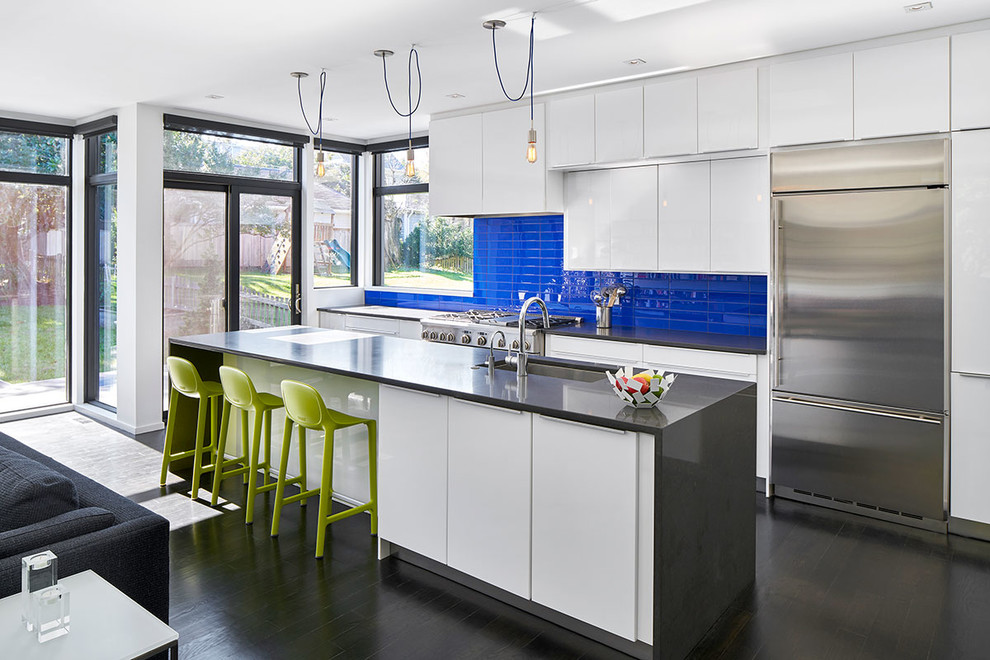Immagine di una cucina design con lavello sottopiano, ante lisce, ante bianche, paraspruzzi blu, paraspruzzi con piastrelle di vetro, elettrodomestici in acciaio inossidabile, parquet scuro e top grigio