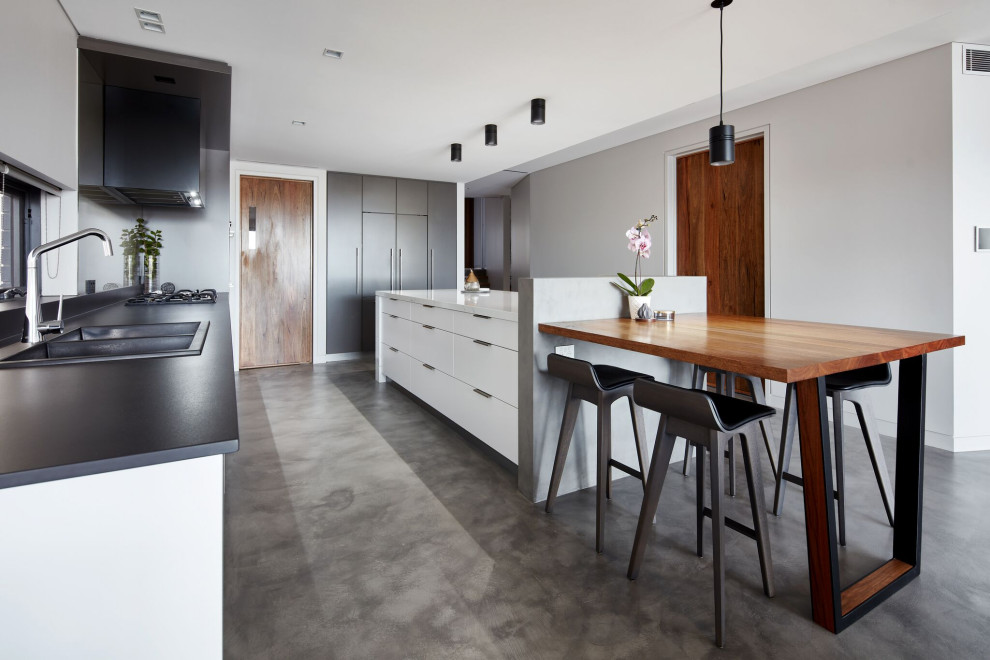 Contemporary kitchen in Sydney with a double-bowl sink, flat-panel cabinets, concrete flooring, an island, grey floors and black worktops.
