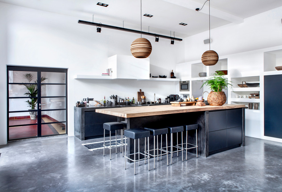 Foto på ett industriellt kök, med släta luckor, blå skåp, vitt stänkskydd, rostfria vitvaror, betonggolv, en köksö och grått golv