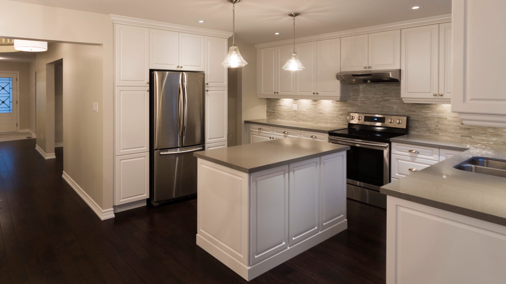 Idéer för ett mellanstort klassiskt grå kök, med en dubbel diskho, luckor med upphöjd panel, vita skåp, bänkskiva i kvarts, grått stänkskydd, stänkskydd i glaskakel, rostfria vitvaror, mörkt trägolv, en köksö och brunt golv