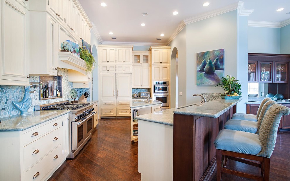 Example of a large beach style medium tone wood floor open concept kitchen design in Miami with white cabinets, granite countertops, blue backsplash, mosaic tile backsplash, stainless steel appliances, an island and a triple-bowl sink