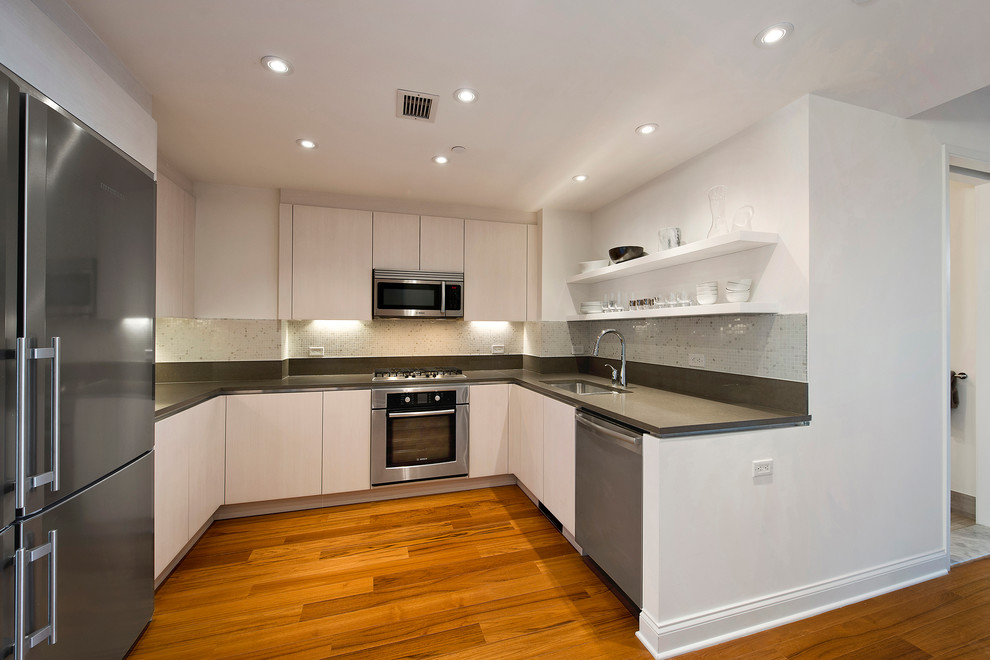 Moderne Küche in U-Form mit flächenbündigen Schrankfronten, weißen Schränken, Quarzit-Arbeitsplatte, Küchengeräten aus Edelstahl und braunem Holzboden in New York