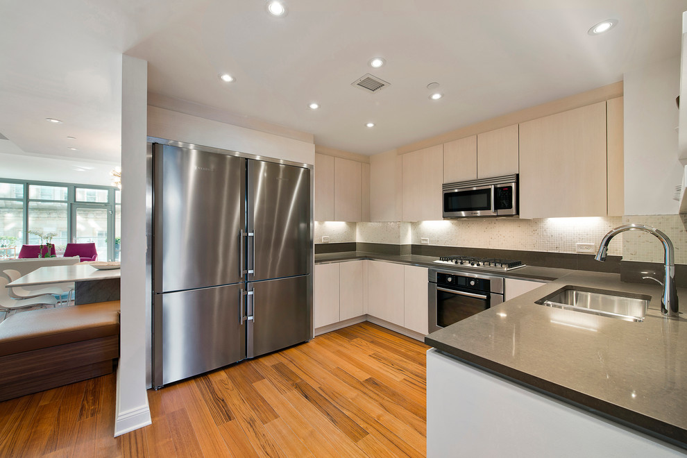 Contemporary u-shaped kitchen in New York with flat-panel cabinets, white cabinets, quartz worktops, stainless steel appliances and medium hardwood flooring.