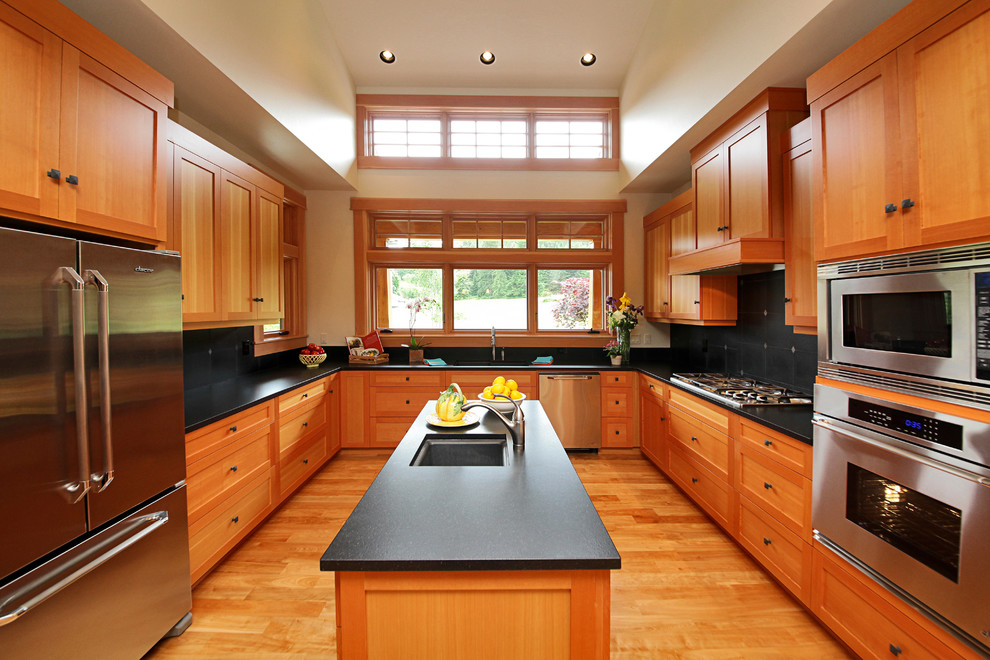 Photo of a medium sized traditional u-shaped enclosed kitchen in Seattle with a submerged sink, shaker cabinets, light wood cabinets, engineered stone countertops, black splashback, stone slab splashback, stainless steel appliances, light hardwood flooring, an island, brown floors and black worktops.