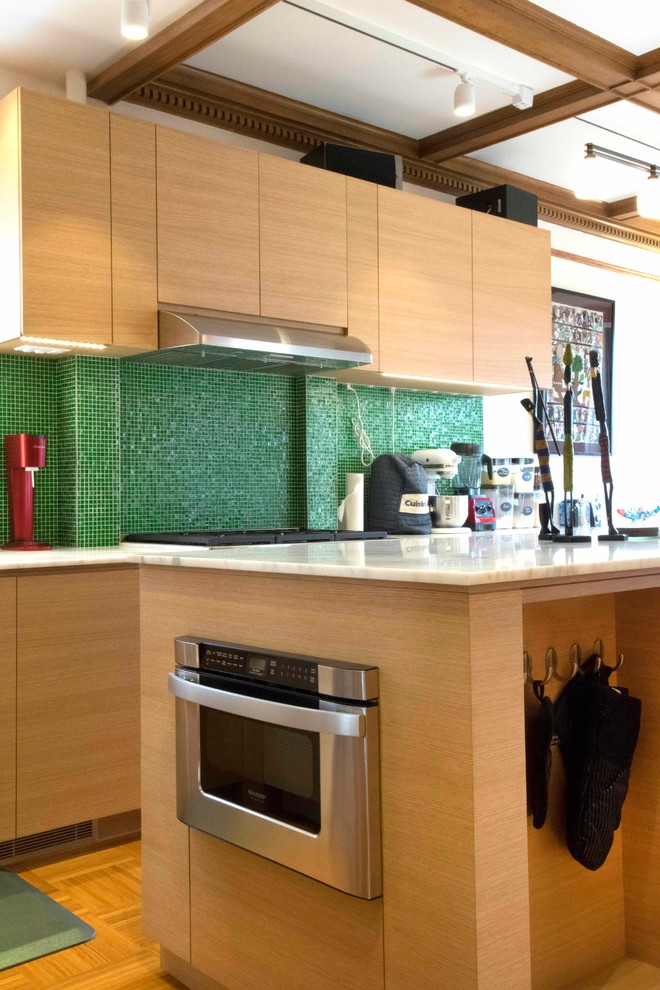 Example of a large 1960s u-shaped medium tone wood floor eat-in kitchen design in New York with an island, an undermount sink, flat-panel cabinets, light wood cabinets, marble countertops, green backsplash, glass tile backsplash and stainless steel appliances