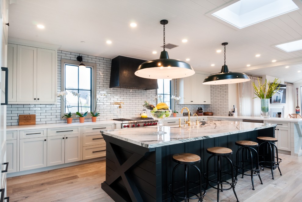 This is an example of a classic u-shaped kitchen in Los Angeles with a belfast sink, shaker cabinets, white cabinets, white splashback, metro tiled splashback, medium hardwood flooring and an island.