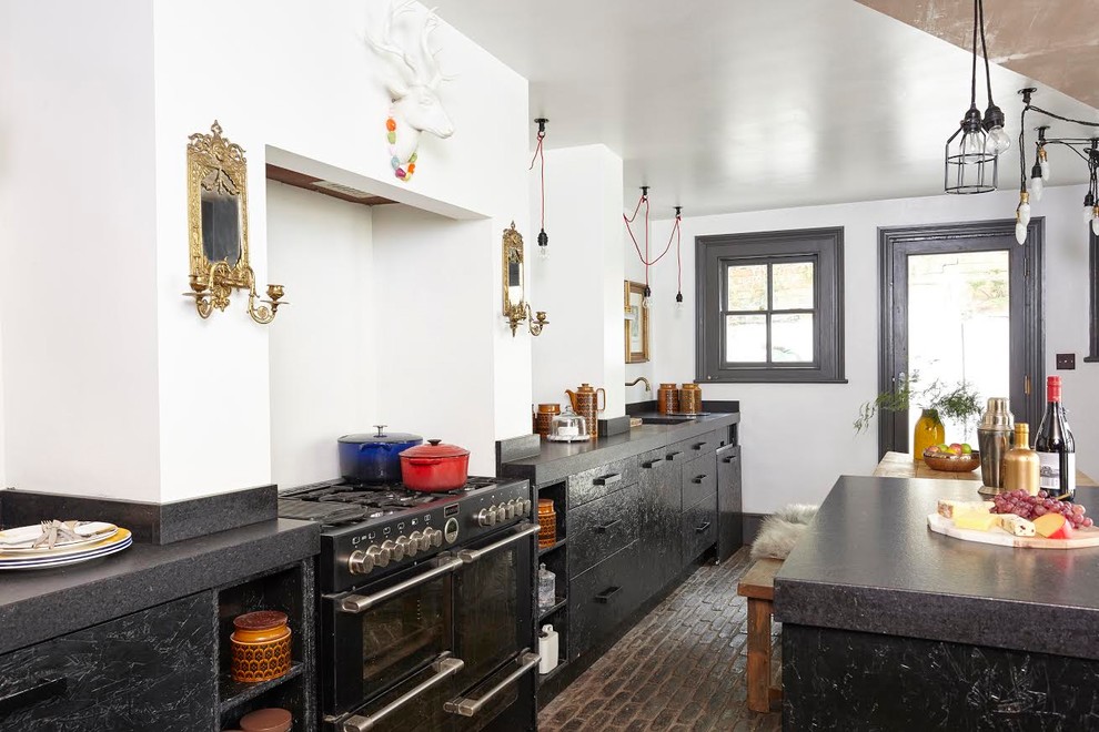 Modelo de cocina comedor de estilo de casa de campo con fregadero de un seno, puertas de armario negras, electrodomésticos negros, suelo de ladrillo y una isla