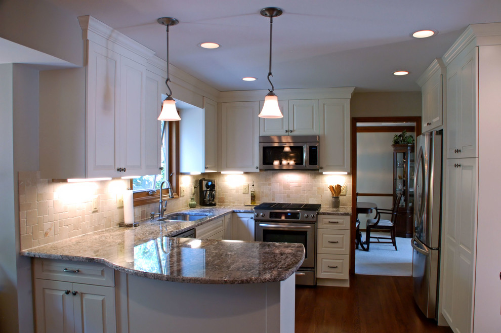 Klassisk inredning av ett mellanstort kök, med en undermonterad diskho, luckor med upphöjd panel, vita skåp, granitbänkskiva, beige stänkskydd, stänkskydd i stenkakel, rostfria vitvaror, mellanmörkt trägolv och en halv köksö