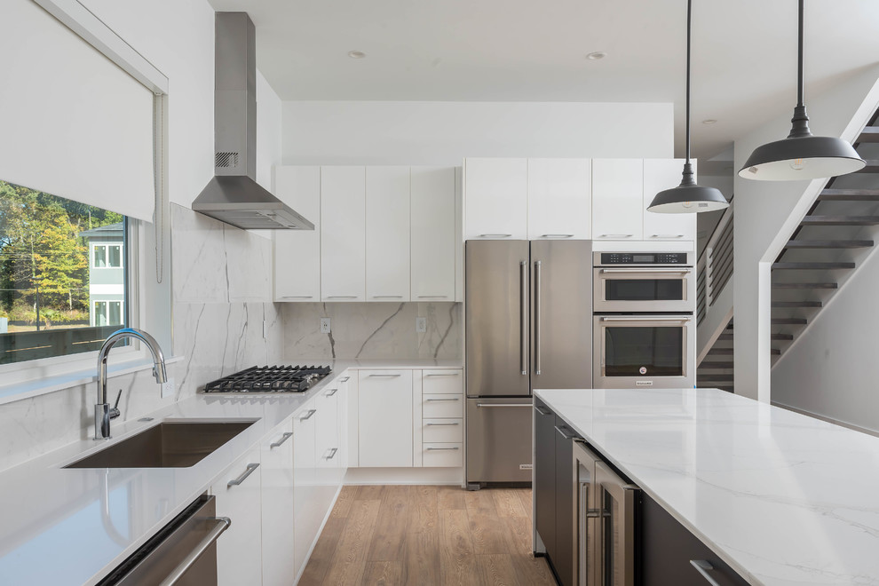 Modern inredning av ett mellanstort kök, med en enkel diskho, släta luckor, vita skåp, bänkskiva i kvarts, vitt stänkskydd, stänkskydd i sten, rostfria vitvaror, ljust trägolv, en köksö och brunt golv