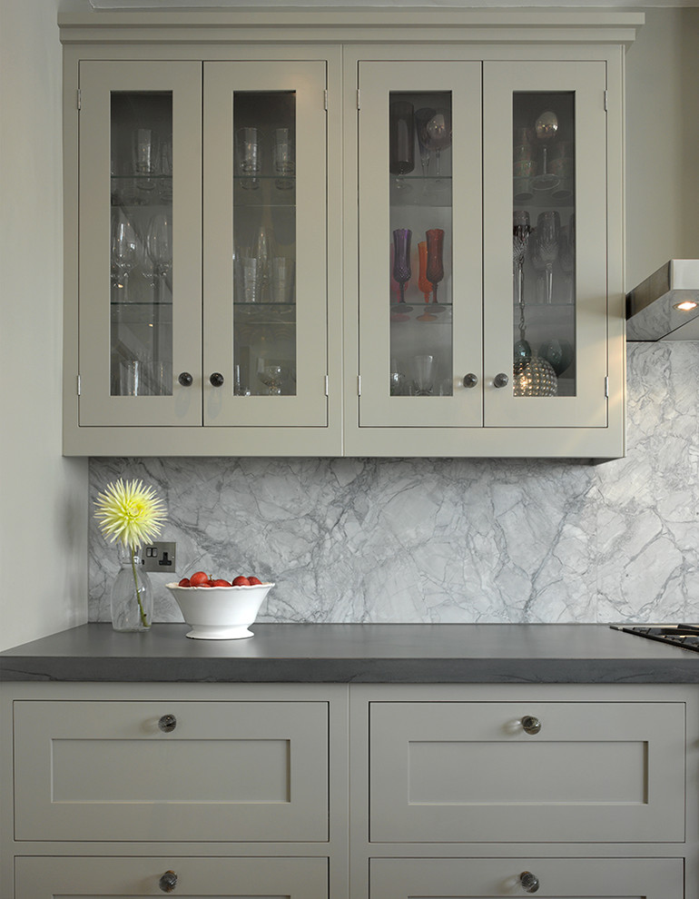 Inspiration for a medium sized contemporary l-shaped enclosed kitchen in London with glass-front cabinets, grey cabinets, white splashback, marble splashback, stainless steel appliances, medium hardwood flooring, an island, beige floors and black worktops.