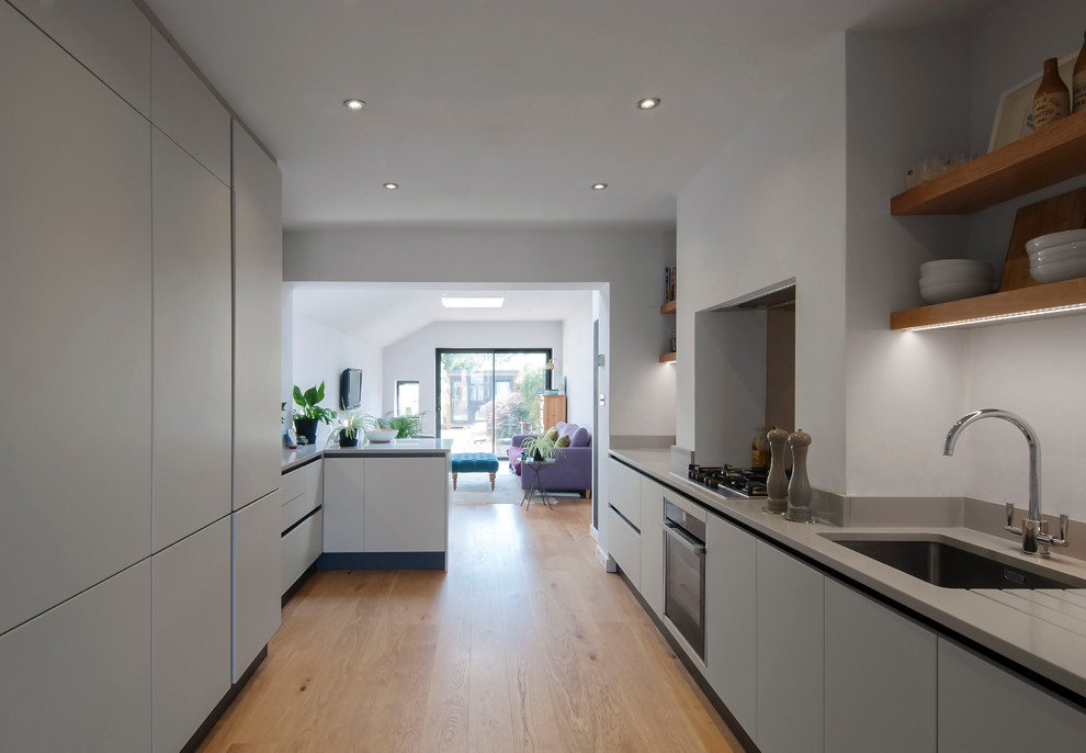 Kleine, Offene, Zweizeilige Moderne Küche mit braunem Holzboden, flächenbündigen Schrankfronten und Mineralwerkstoff-Arbeitsplatte in London