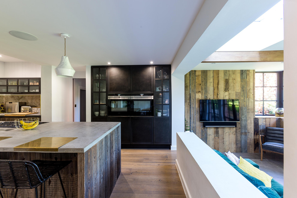 Medium sized contemporary l-shaped open plan kitchen in Hertfordshire with an integrated sink, flat-panel cabinets, medium wood cabinets, composite countertops, multi-coloured splashback, cement tile splashback, black appliances, medium hardwood flooring, an island, brown floors and grey worktops.