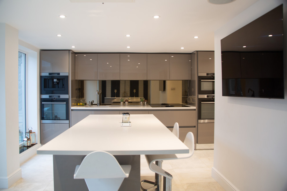 Medium sized contemporary single-wall kitchen in Hertfordshire with a submerged sink, flat-panel cabinets, grey cabinets, metallic splashback, glass sheet splashback, stainless steel appliances, an island, beige floors and white worktops.