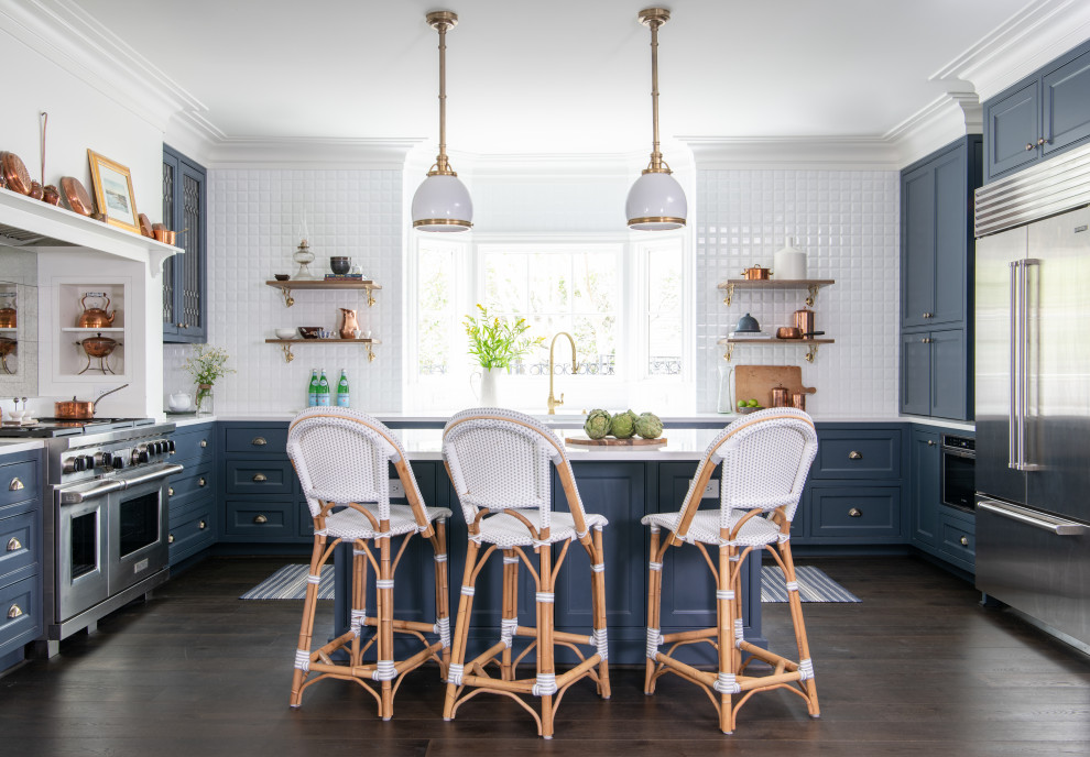 Example of a classic u-shaped dark wood floor and brown floor kitchen design in Houston with a farmhouse sink, blue cabinets, white backsplash, stainless steel appliances, an island, white countertops and beaded inset cabinets