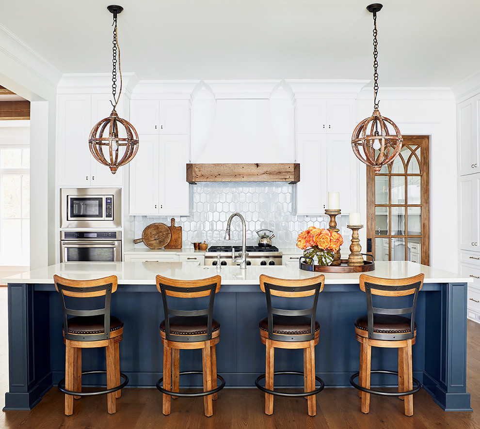 Inspiration for a beach style kitchen in Raleigh with shaker cabinets, white cabinets, white splashback, stainless steel appliances, medium hardwood flooring, an island and white worktops.