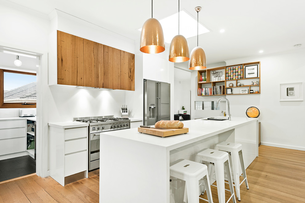 Bild på ett mellanstort funkis vit vitt kök, med en undermonterad diskho, släta luckor, vita skåp, bänkskiva i kvarts, vitt stänkskydd, rostfria vitvaror, mellanmörkt trägolv, en köksö och beiget golv