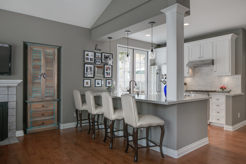 Example of a small trendy galley eat-in kitchen design in Orange County with a farmhouse sink, shaker cabinets, white cabinets, quartz countertops, gray backsplash, mosaic tile backsplash, stainless steel appliances and an island
