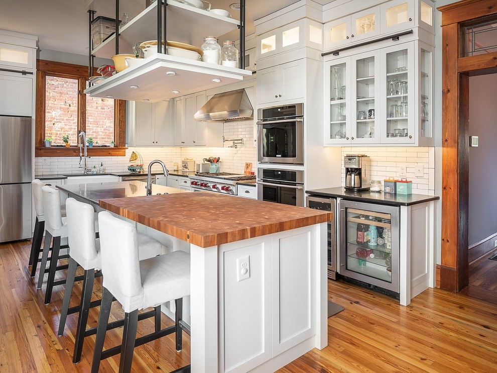 Large traditional l-shaped enclosed kitchen in Atlanta with shaker cabinets, white cabinets, engineered stone countertops, white splashback, metro tiled splashback, stainless steel appliances, an island, brown floors, black worktops, a belfast sink and medium hardwood flooring.