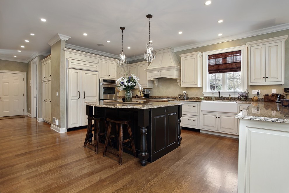 Diseño de cocina clásica, de tamaño medio, con fregadero sobremueble, armarios con paneles con relieve, puertas de armario beige, encimera de granito, electrodomésticos con paneles, suelo de madera en tonos medios, una isla, suelo marrón y encimeras marrones