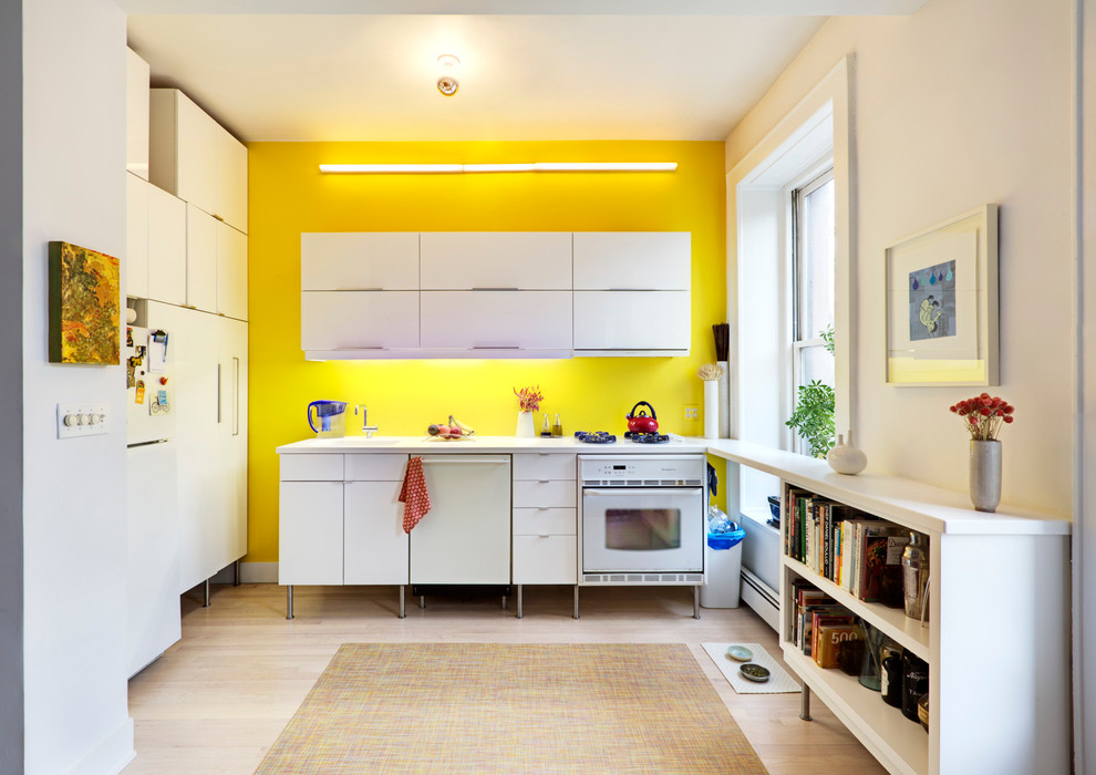 Enclosed kitchen - small contemporary l-shaped light wood floor enclosed kitchen idea in New York with white cabinets, yellow backsplash, white appliances, no island and flat-panel cabinets