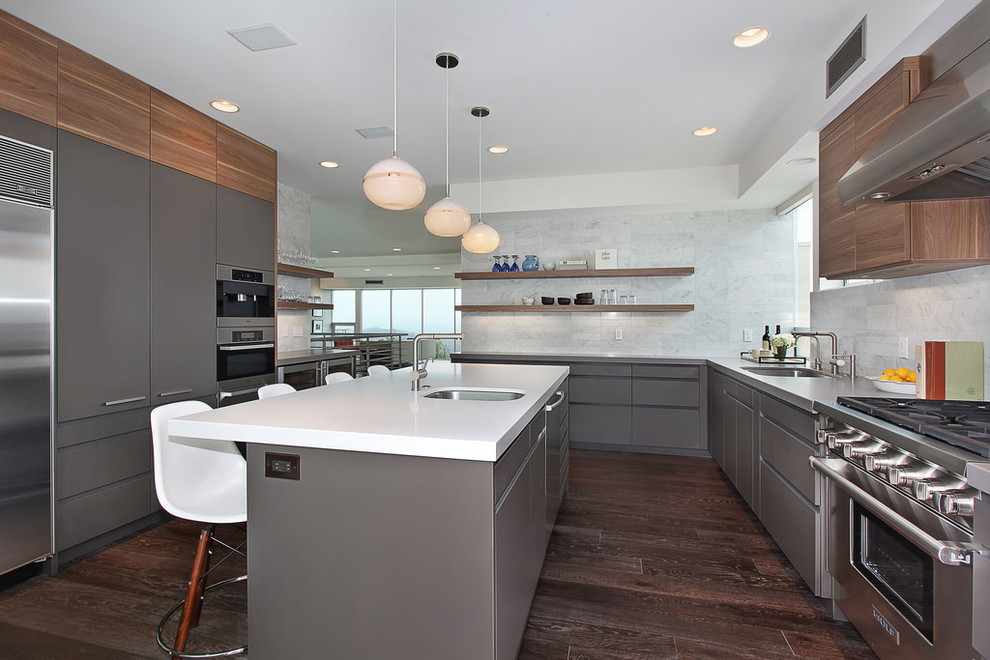 Contemporary u-shaped kitchen in San Diego with a submerged sink, flat-panel cabinets, grey cabinets, stainless steel appliances, dark hardwood flooring, an island, brown floors and white worktops.