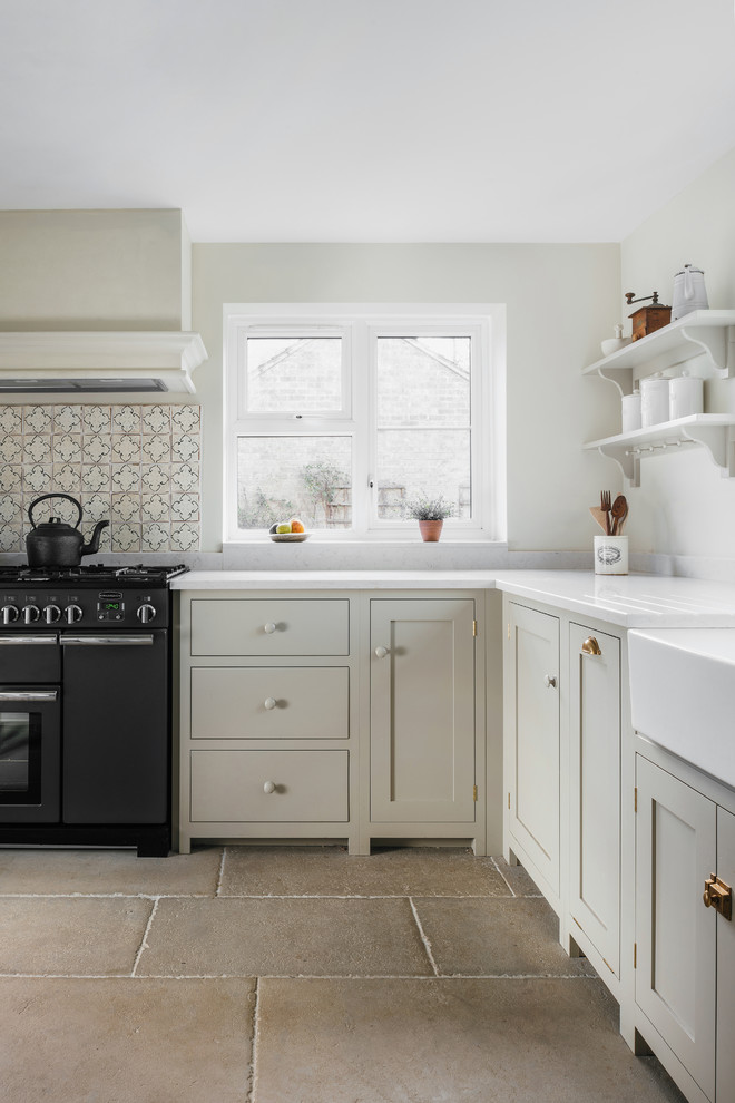 Medium sized traditional l-shaped enclosed kitchen in Cambridgeshire with a belfast sink, shaker cabinets, black appliances, stainless steel cabinets, beige splashback, ceramic splashback and beige floors.