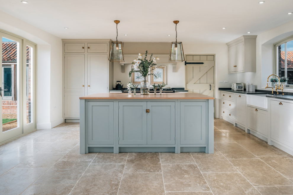 Photo of a medium sized traditional l-shaped kitchen/diner in Cambridgeshire with a belfast sink, shaker cabinets, black appliances, an island, brown floors and beige cabinets.