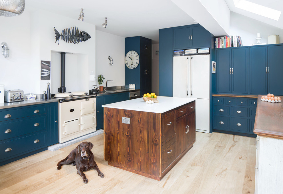Design ideas for a classic kitchen in London with an integrated sink, blue cabinets, stainless steel worktops, white appliances, light hardwood flooring, an island and beige floors.