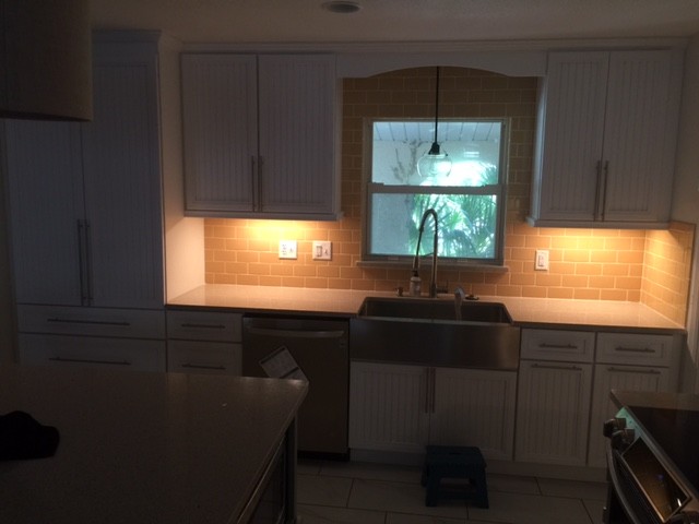 This is an example of a medium sized beach style l-shaped kitchen/diner in Orlando with a belfast sink, louvered cabinets, green cabinets, engineered stone countertops, yellow splashback, metro tiled splashback, stainless steel appliances, porcelain flooring and an island.