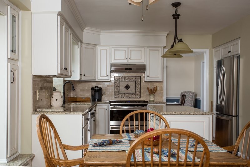 Bild på ett mellanstort vintage kök, med beige stänkskydd, stänkskydd i stenkakel, rostfria vitvaror, mellanmörkt trägolv, en köksö, skåp i shakerstil, vita skåp, granitbänkskiva och en dubbel diskho