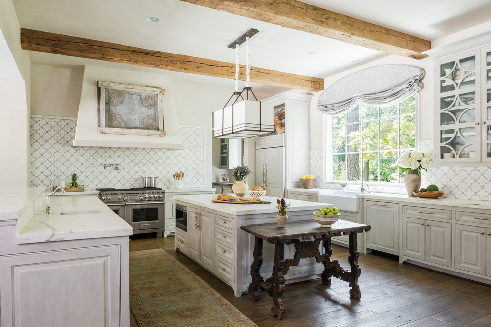Inredning av ett medelhavsstil vit vitt u-kök, med en rustik diskho, luckor med upphöjd panel, grå skåp, vitt stänkskydd, rostfria vitvaror, mörkt trägolv, en köksö och brunt golv